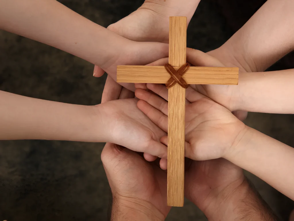 An image showing people holding up a wooden cross together.